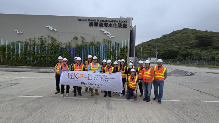Group of engineers in hard hats and safety vests posing with banner outside desalination plant.