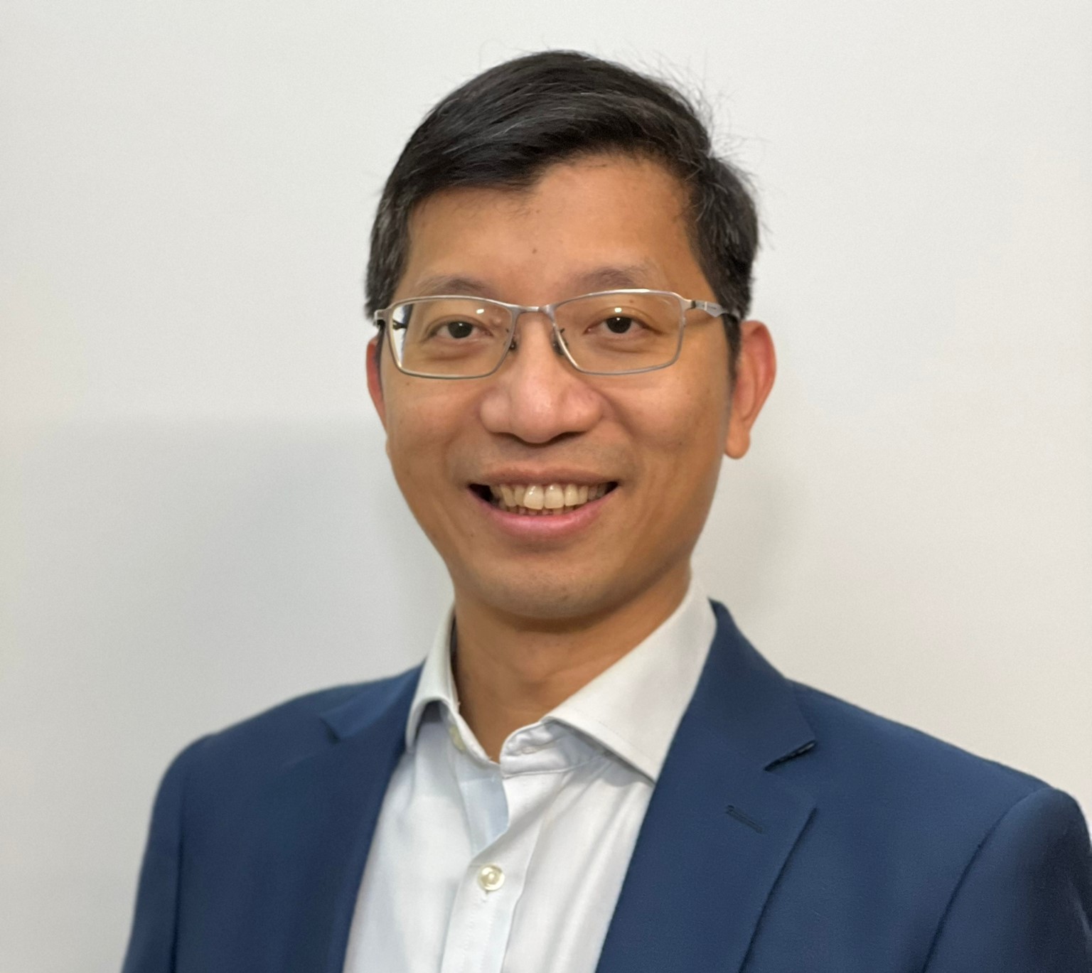 Smiling man with glasses wearing a blue suit and white shirt.
