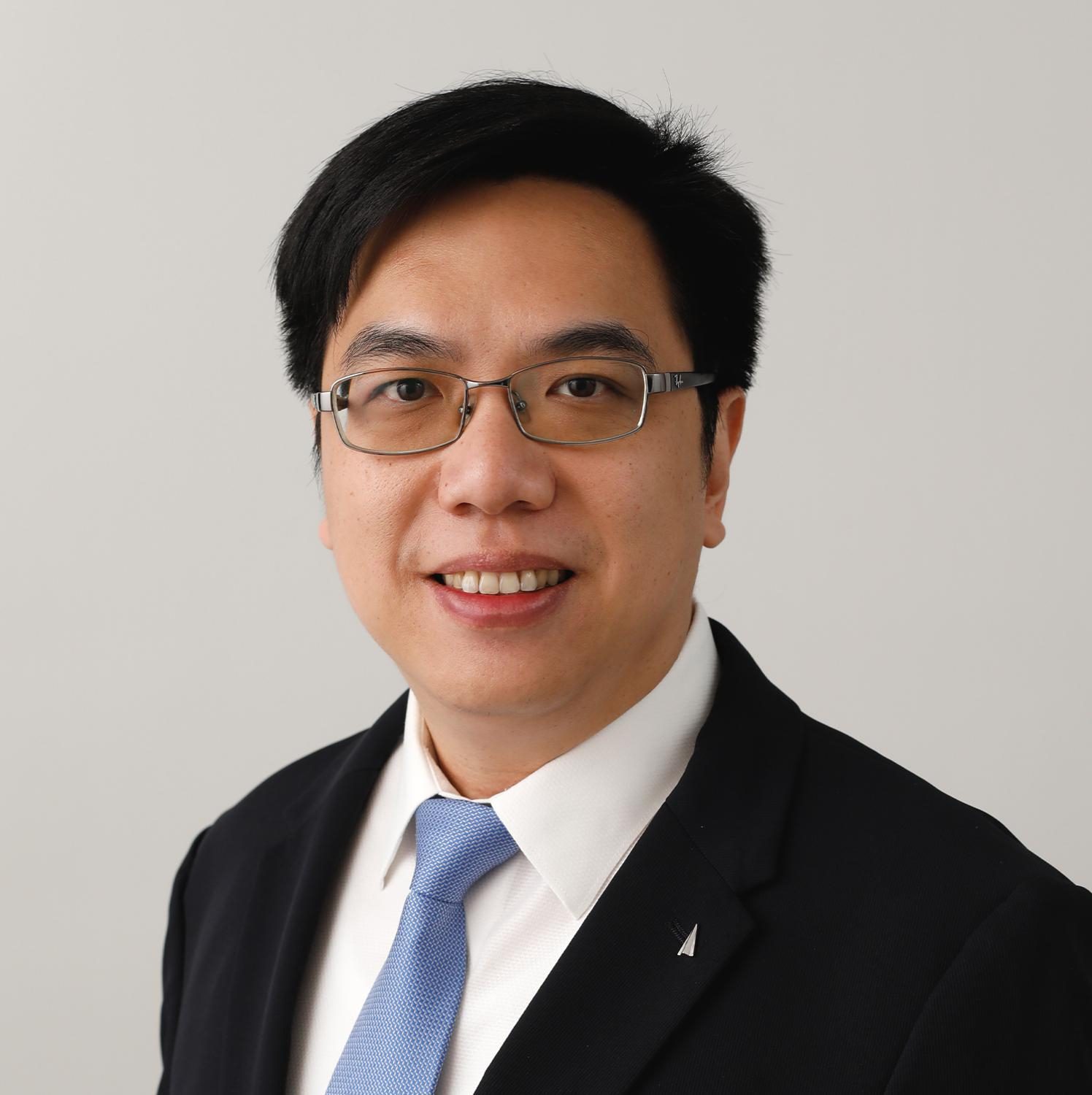 Professional headshot of a smiling man wearing glasses, suit, and blue tie.