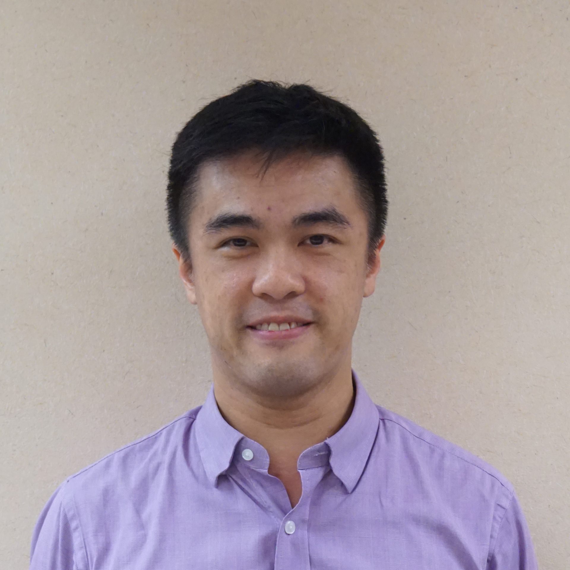 Portrait of a man with short dark hair wearing a purple button-up shirt.