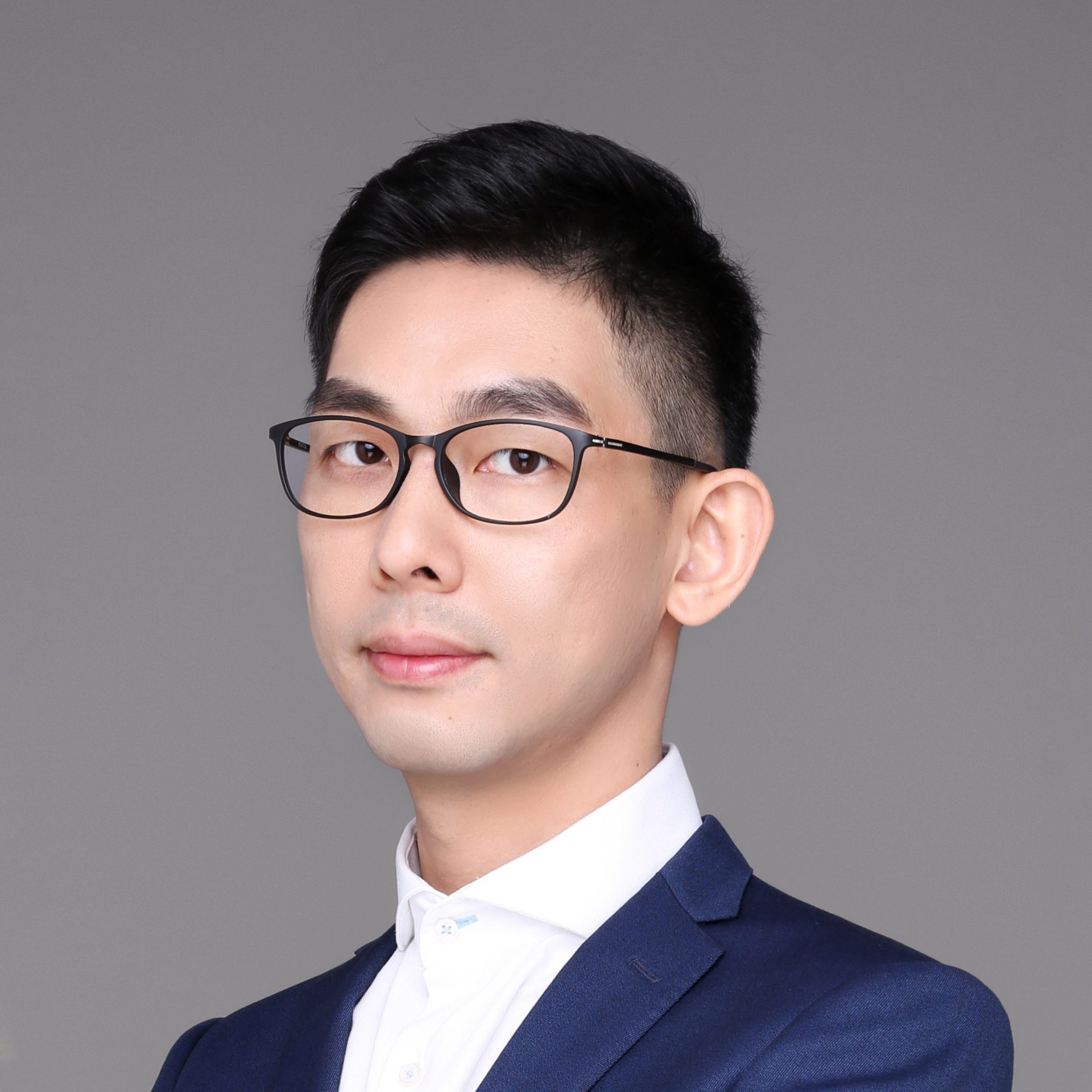 Professional headshot of a man with glasses wearing a blue suit and white shirt.