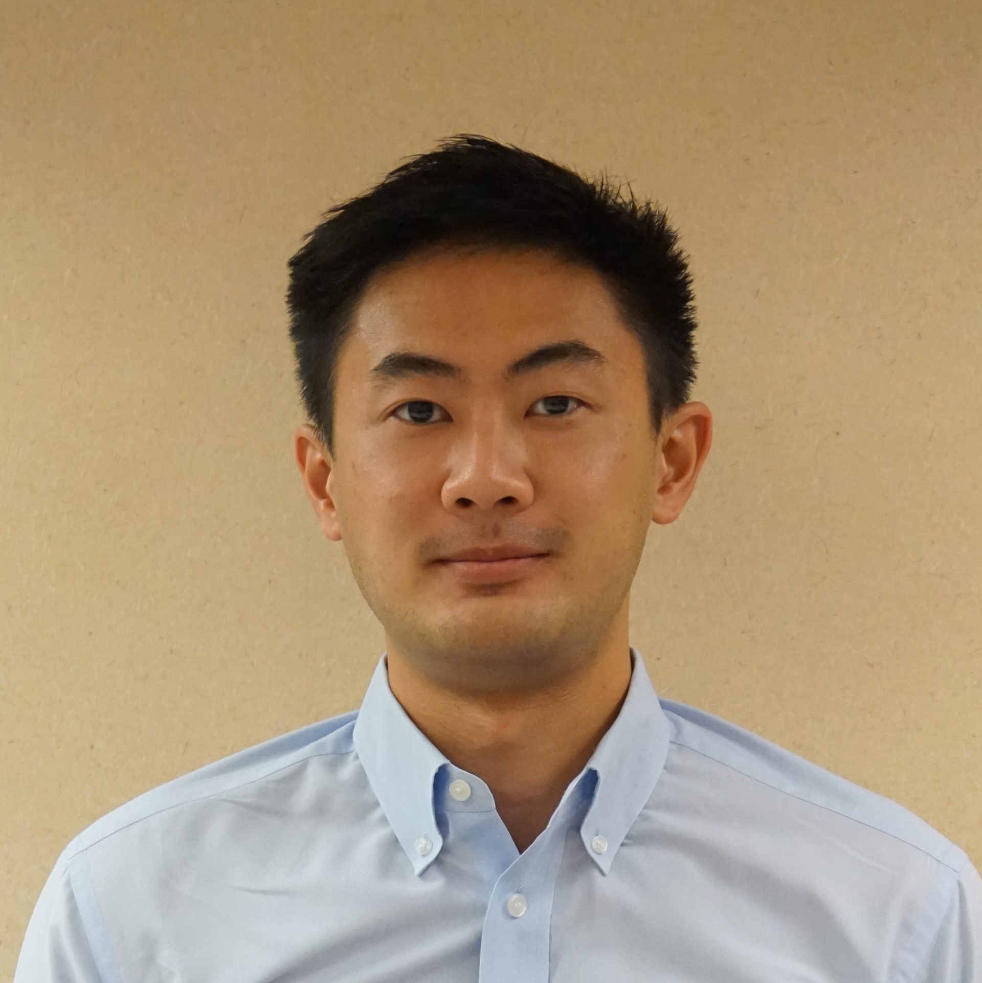 Portrait of a man with short dark hair wearing a light blue button-up shirt.