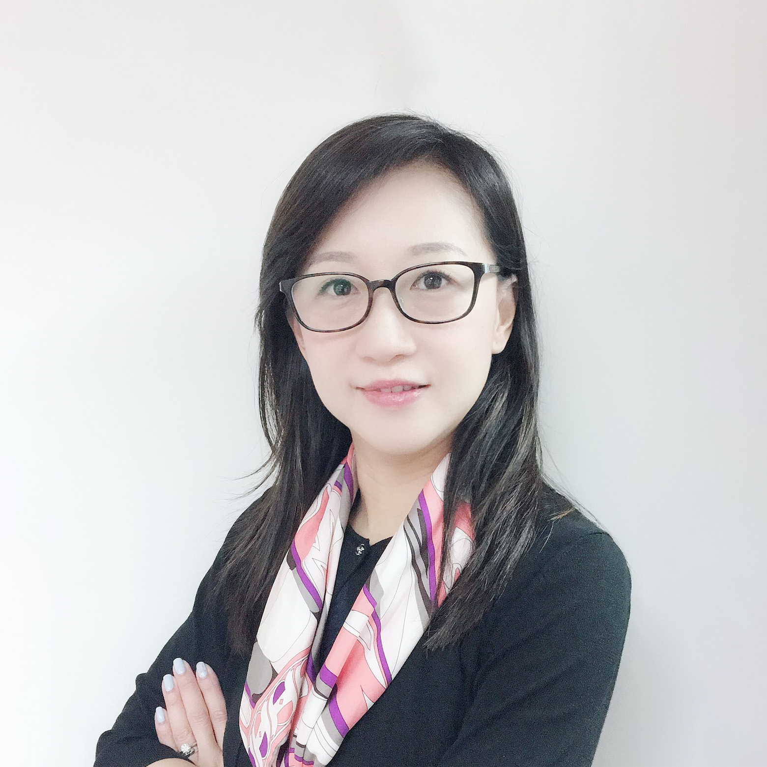 Professional woman with glasses and patterned scarf, arms crossed, smiling at camera.