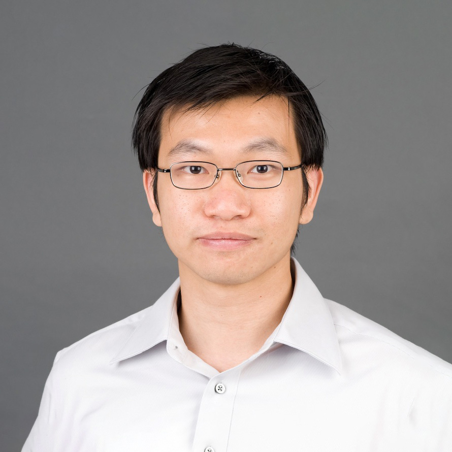 Portrait of a man with glasses wearing a white collared shirt against a gray background.