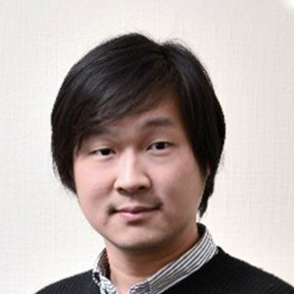 Portrait of a man with dark hair wearing a striped shirt and dark sweater.