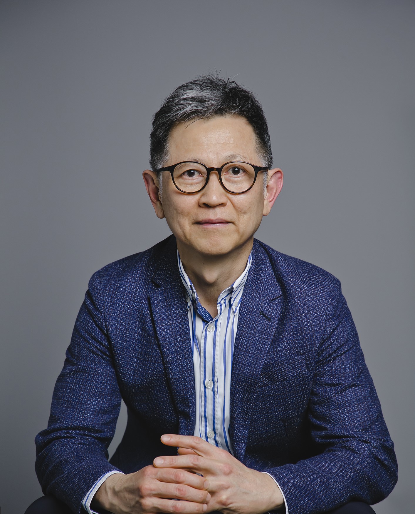 Portrait of a man with glasses wearing a blue blazer and striped shirt.