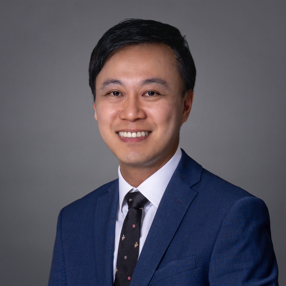 Professional headshot of a smiling man in a blue suit and patterned tie.