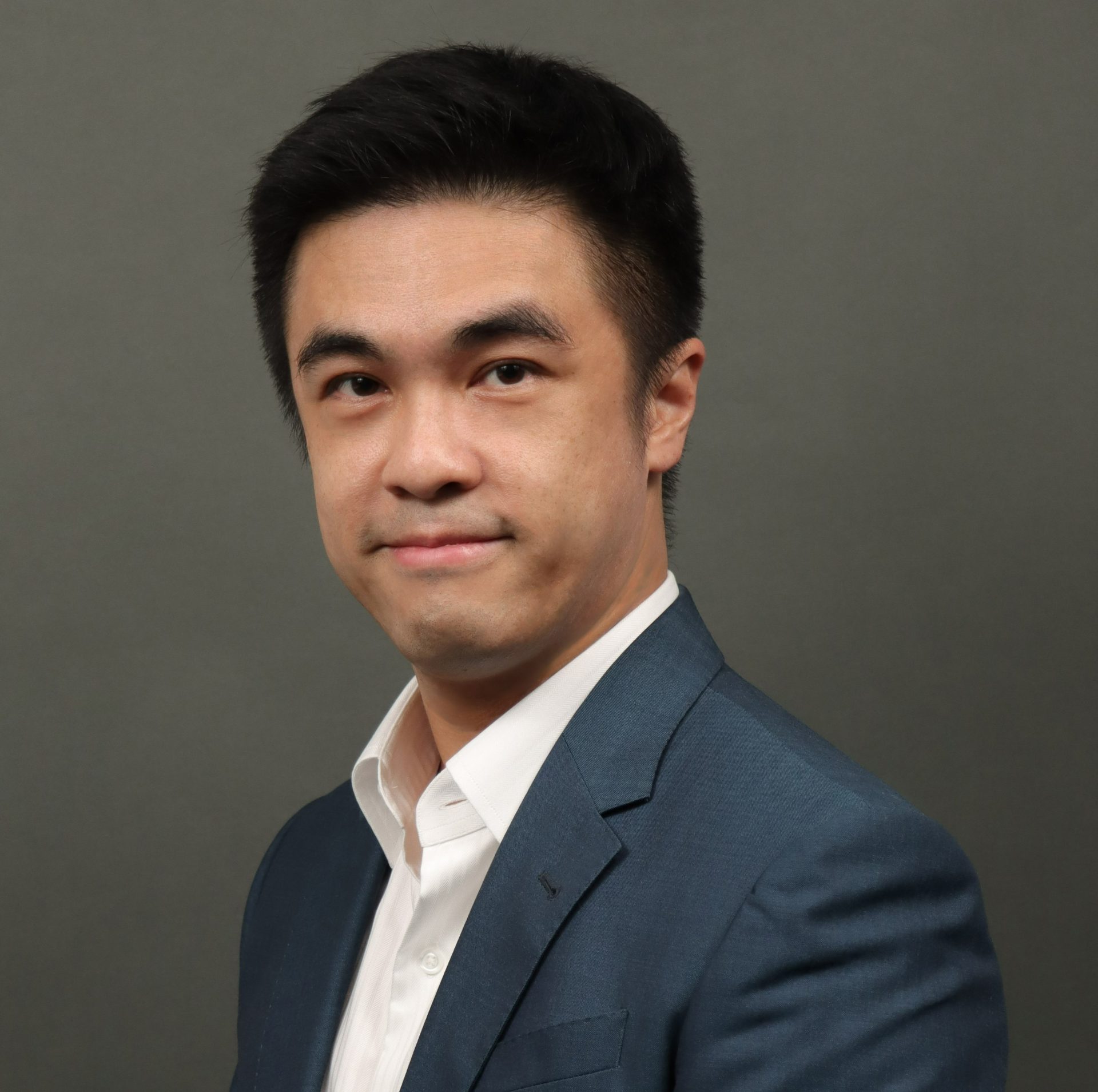 Portrait of a man in a blue suit and white shirt against a gray background.