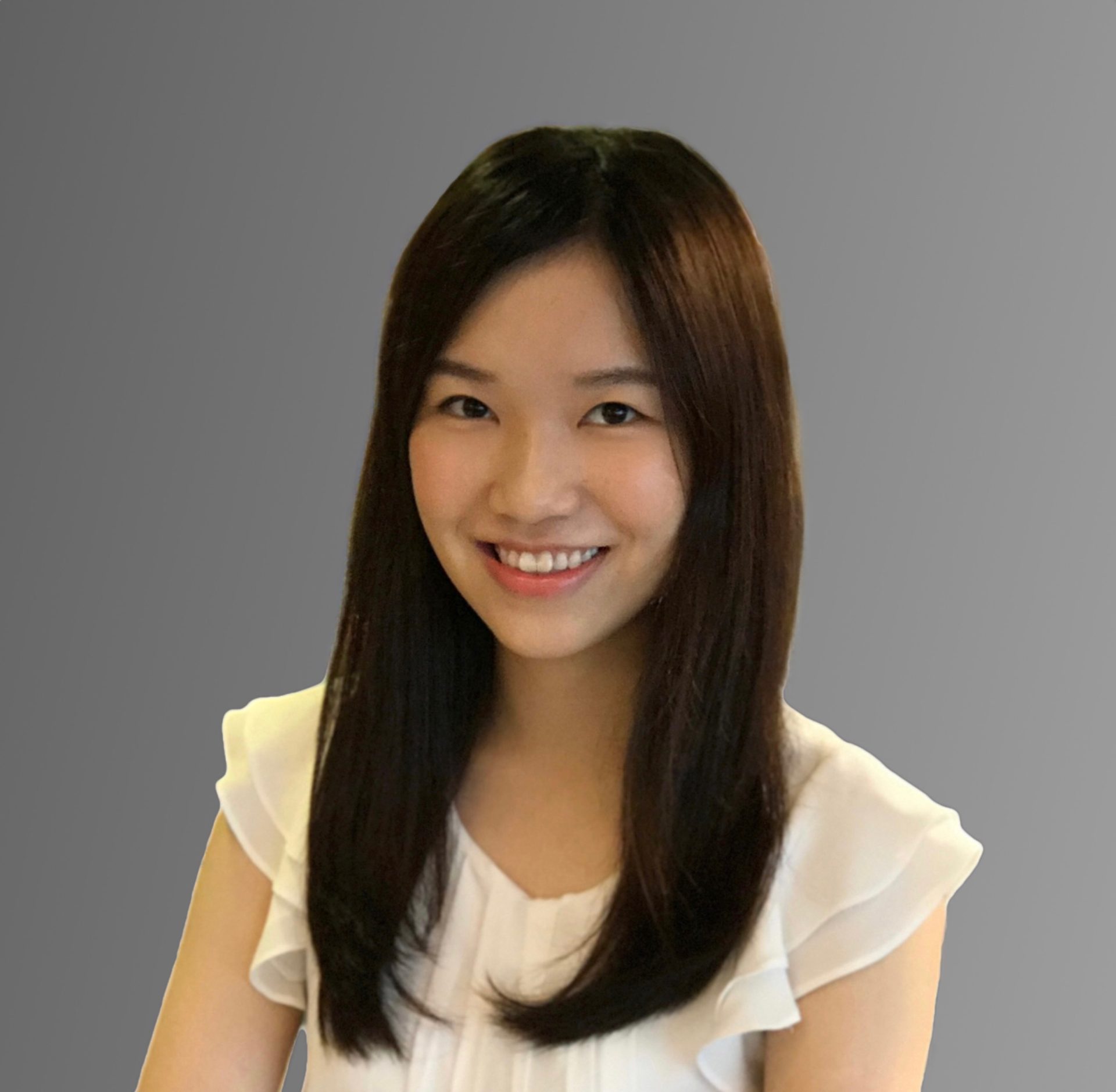 Smiling woman with long dark hair wearing a white blouse against a gray background.