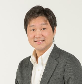 Smiling East Asian man in gray blazer and white shirt against plain background
