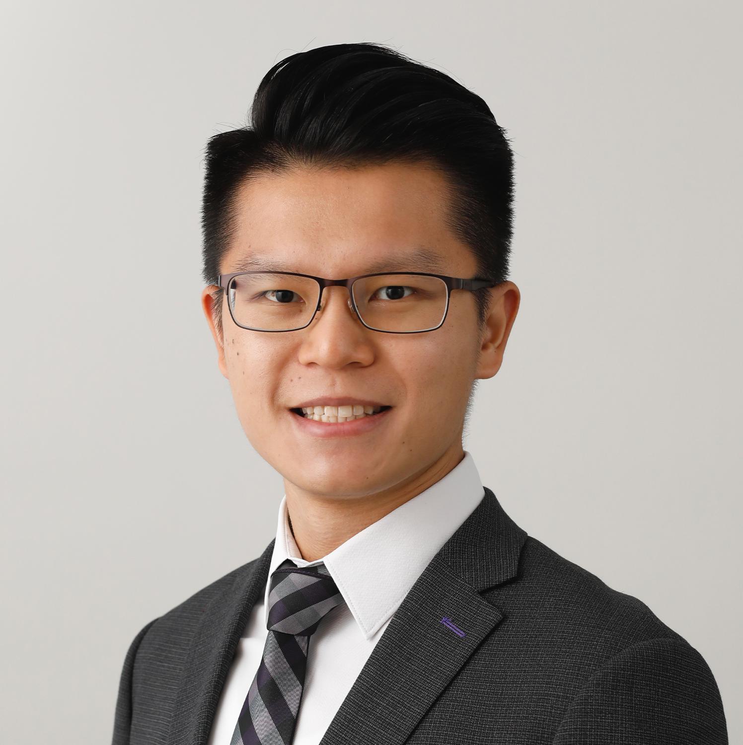 Professional headshot of a smiling man wearing glasses, suit, and tie.