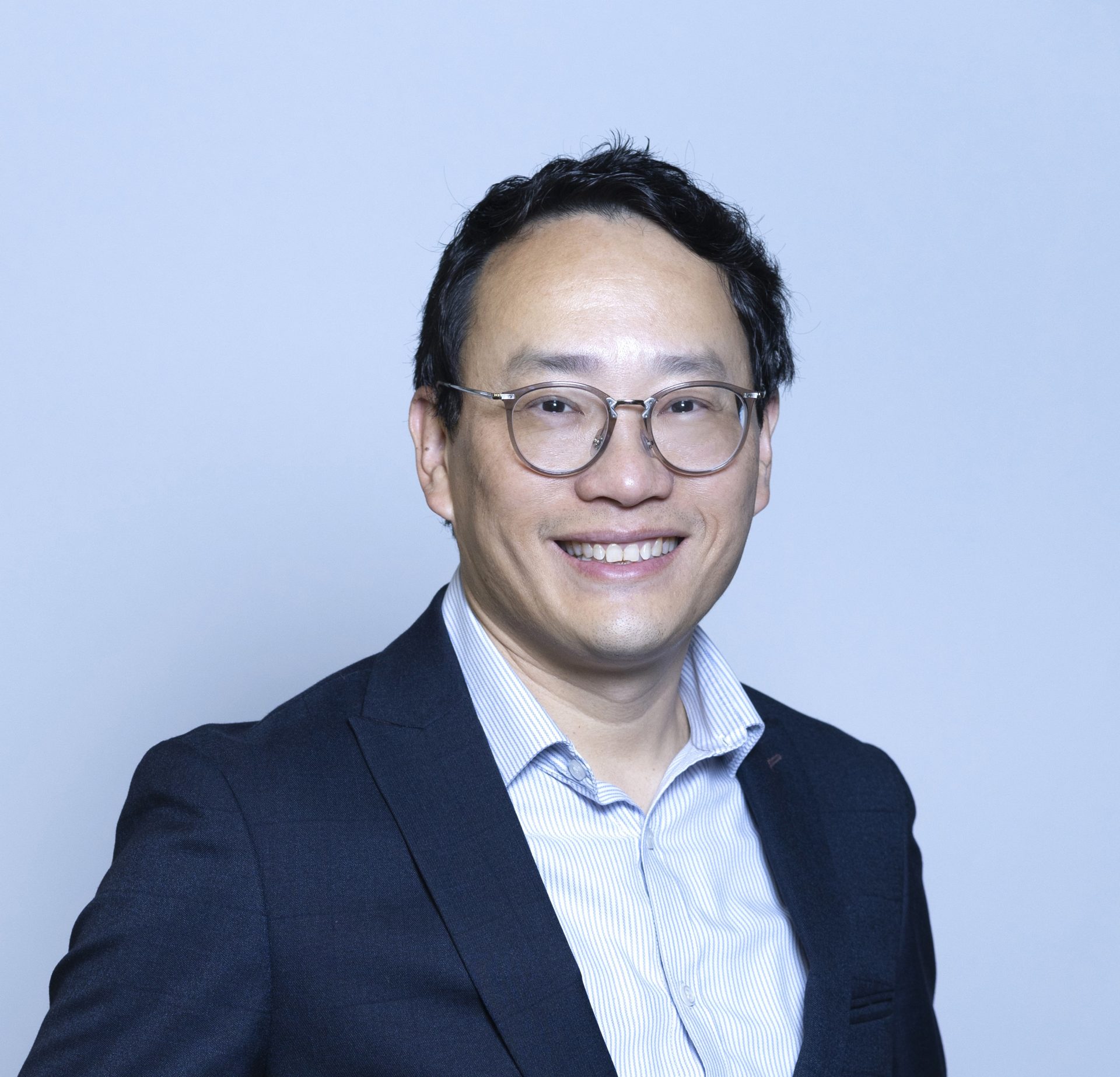 Smiling man with glasses wearing a suit and striped shirt.