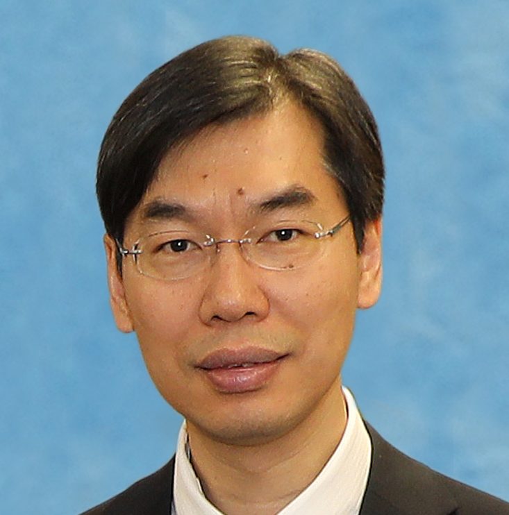 Headshot of a man with glasses wearing a suit and white shirt against a blue background.