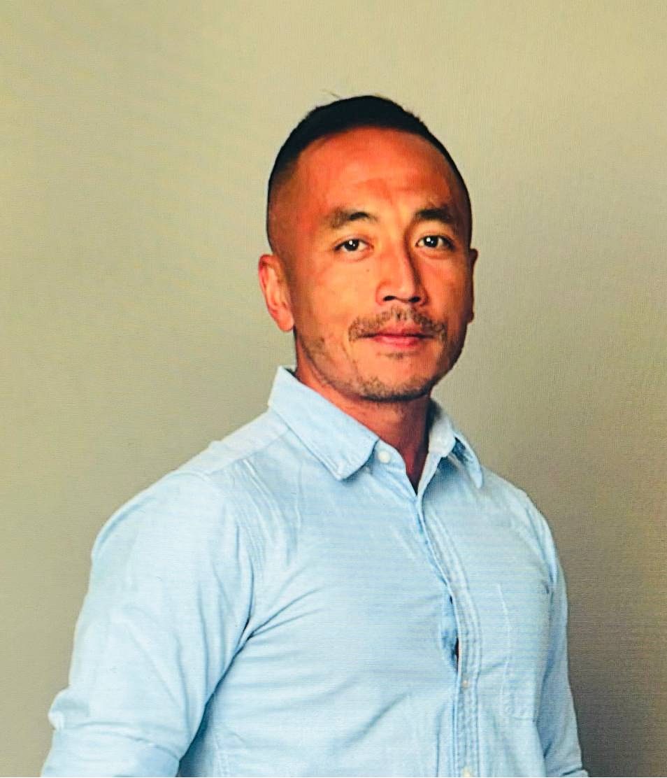 Portrait of a man with short dark hair and mustache wearing a light blue button-up shirt.