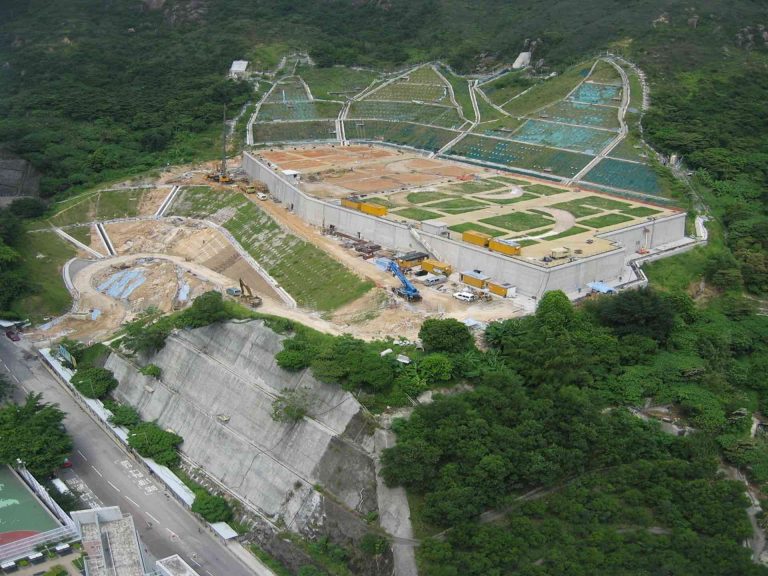 Aerial view of a large construction site nestled in a lush, hilly landscape with heavy machinery and terraced earthworks.
