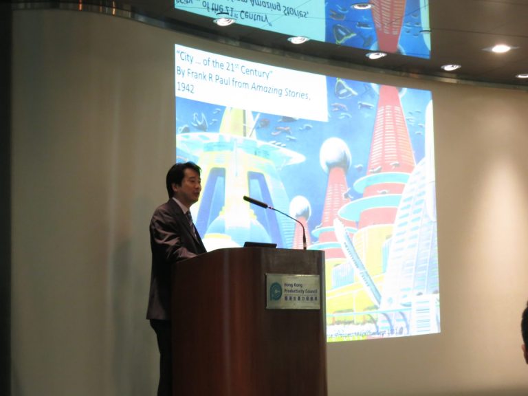 Man speaking at podium with futuristic city illustration on screen behind him.