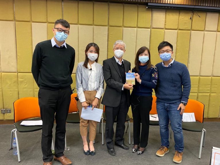 Five people wearing masks stand together, two holding a book.