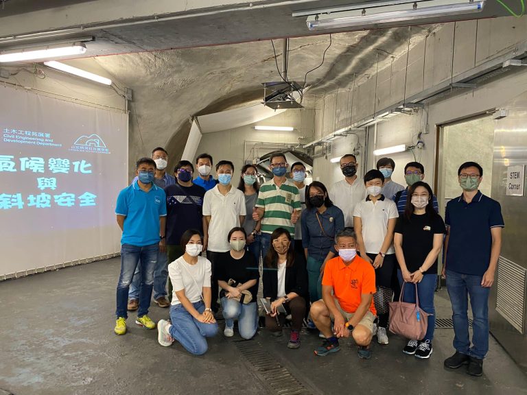 Group photo of people wearing masks inside a tunnel with a presentation screen in the background.