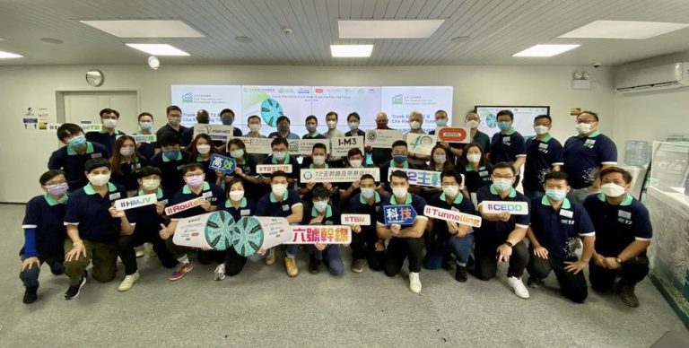 Group of people in matching uniforms holding signs with text and logos, wearing face masks indoors.
