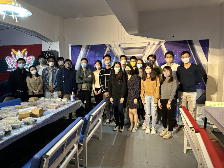 Group of people wearing face masks posing for a photo in a room with a space-themed backdrop.