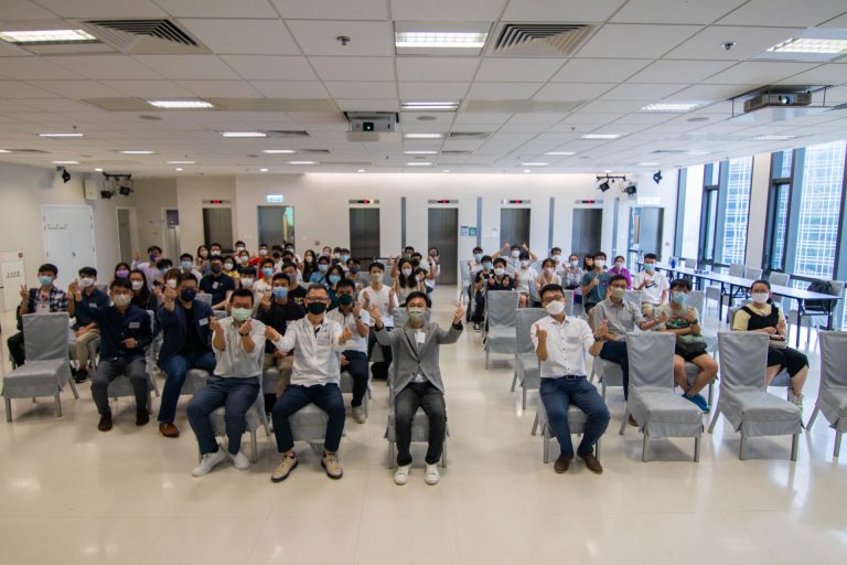 Group of people wearing masks and seated in a room, making hand gestures.