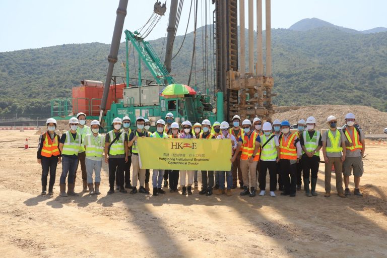 Group of engineers in safety gear holding HKIE Geotechnical Division banner at construction site.