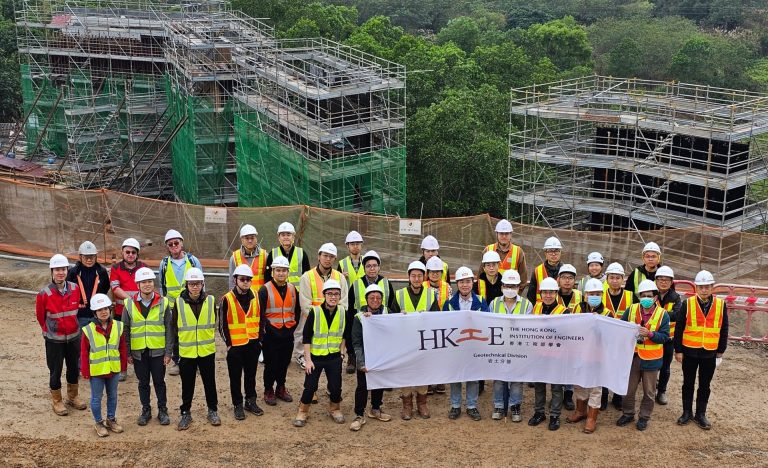 Group of engineers in safety gear posing with HKIE Geotechnical Division banner at construction site.