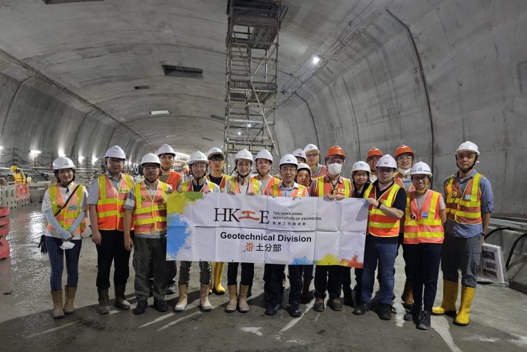 Group of engineers in hard hats and safety vests posing with banner in a tunnel.