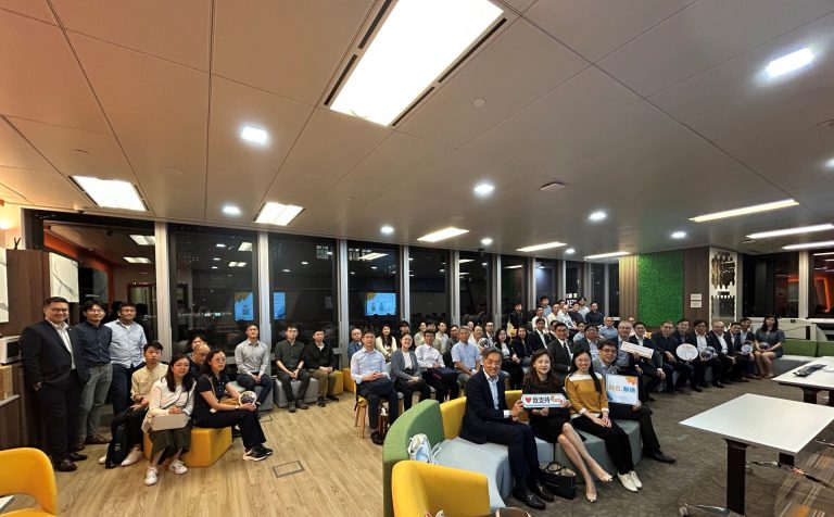 Group of people posing for photo in modern office lounge with colorful seating and large windows.