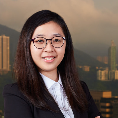 Professional portrait of a smiling woman with glasses against a cityscape background.