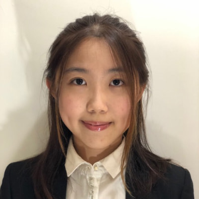 Young woman with long brown hair wearing a white collared shirt and dark blazer, smiling at the camera.