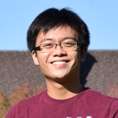 Smiling man with glasses wearing maroon shirt outdoors