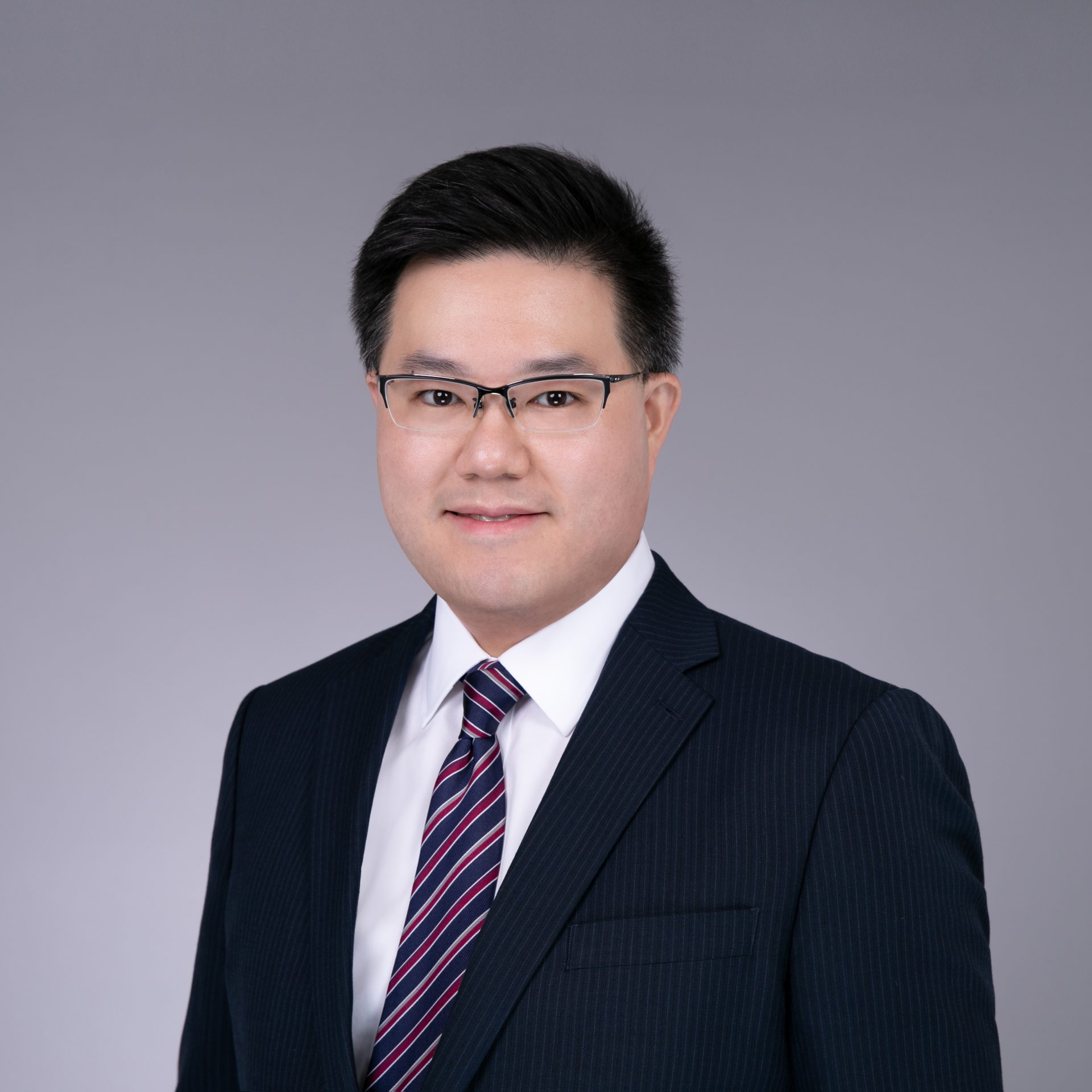 Professional headshot of a man wearing glasses, a dark pinstripe suit, and a striped tie.