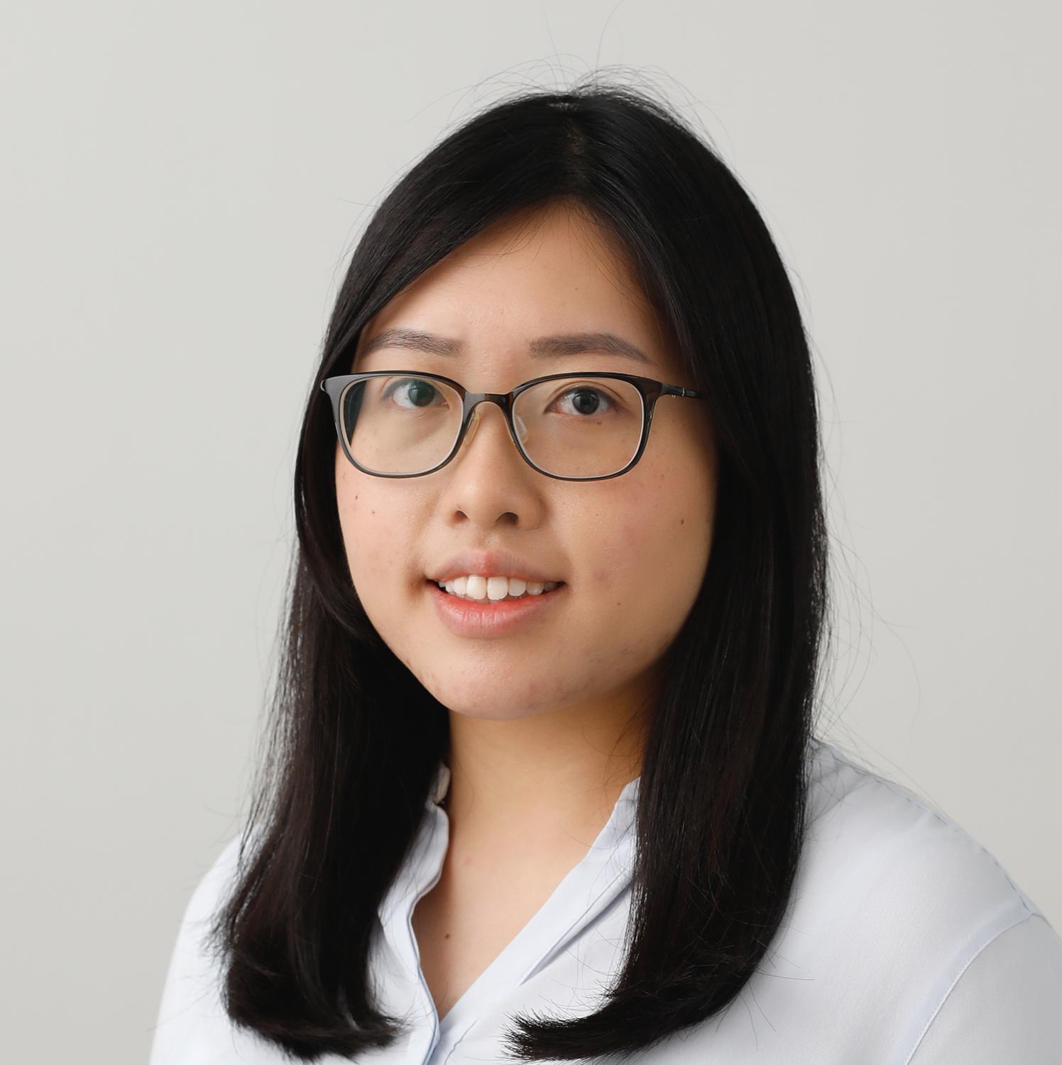 Portrait of a woman with dark hair and glasses wearing a light blue collared shirt.