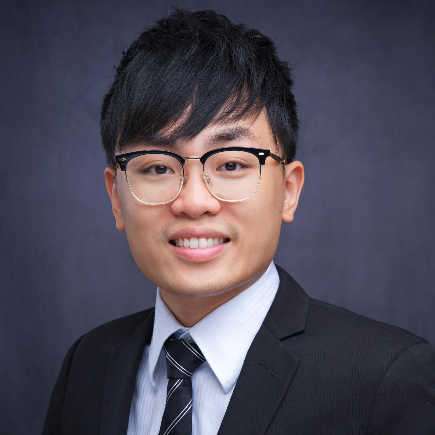Portrait of a smiling man wearing glasses, suit, and striped tie.