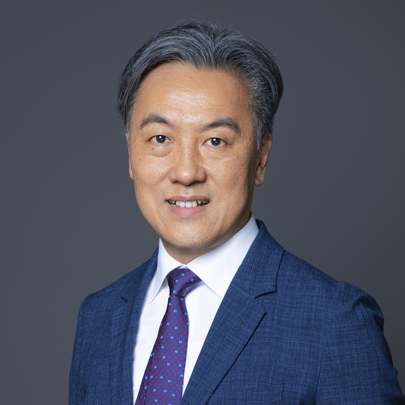 Portrait of a smiling man in a blue suit and patterned tie.