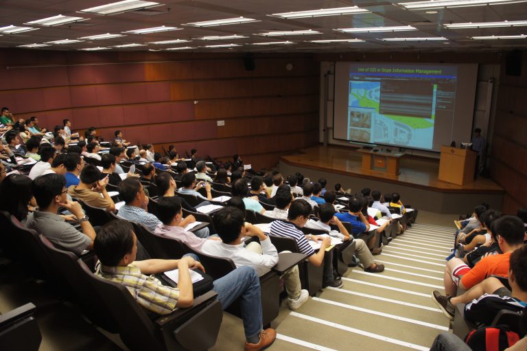 Audience attending lecture on GIS in slope management, viewing presentation on stage.