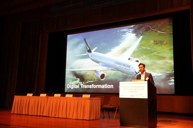 "Speaker presents at conference with slide showing Cathay Pacific airplane and ""Digital Transformation"" text."