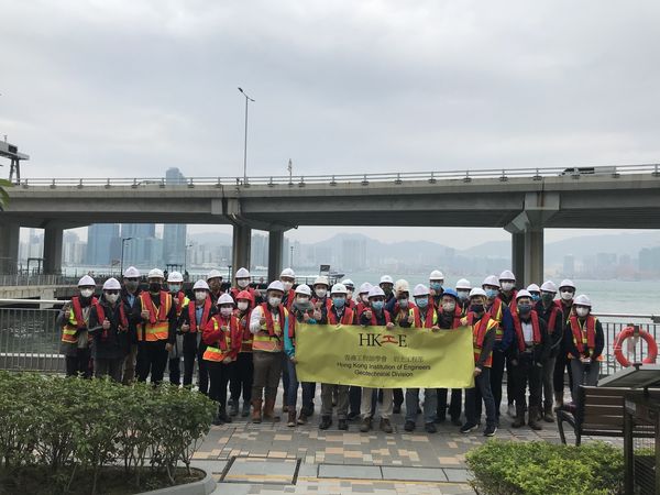 Group of construction workers in hard hats and safety vests holding a HKIE banner under a bridge.