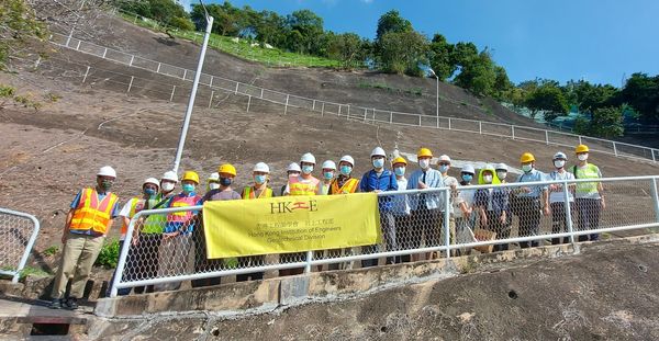 Group of engineers in safety gear posing with HKIE banner at construction site