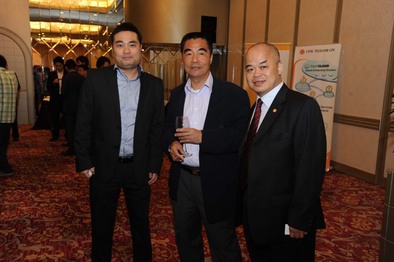 "Three men in suits posing at a business event with a ""CITIC TELECOM CPC"" banner in the background."