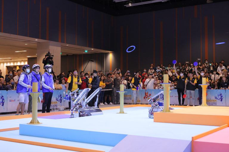 Robotic arms compete in Robocon Hong Kong 2023, with spectators watching and cheering.