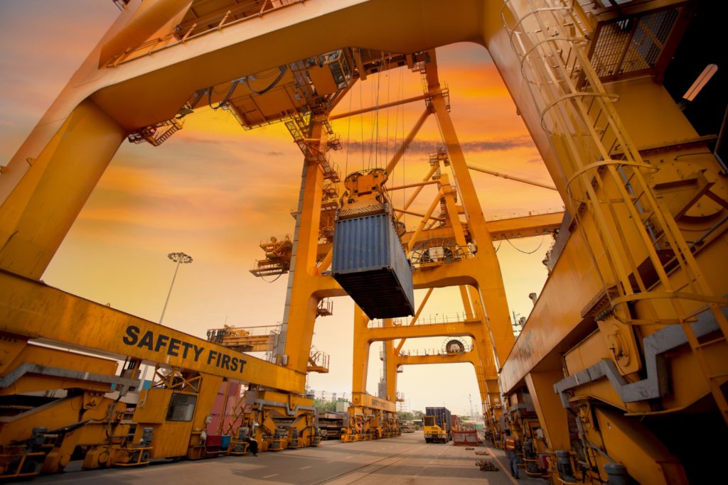 Large yellow port cranes lifting a shipping container at sunset.