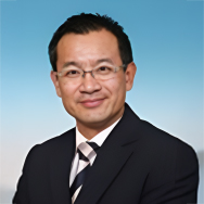 Portrait of Ir Alan Tam, wearing glasses and suit, smiling against blue gradient background.