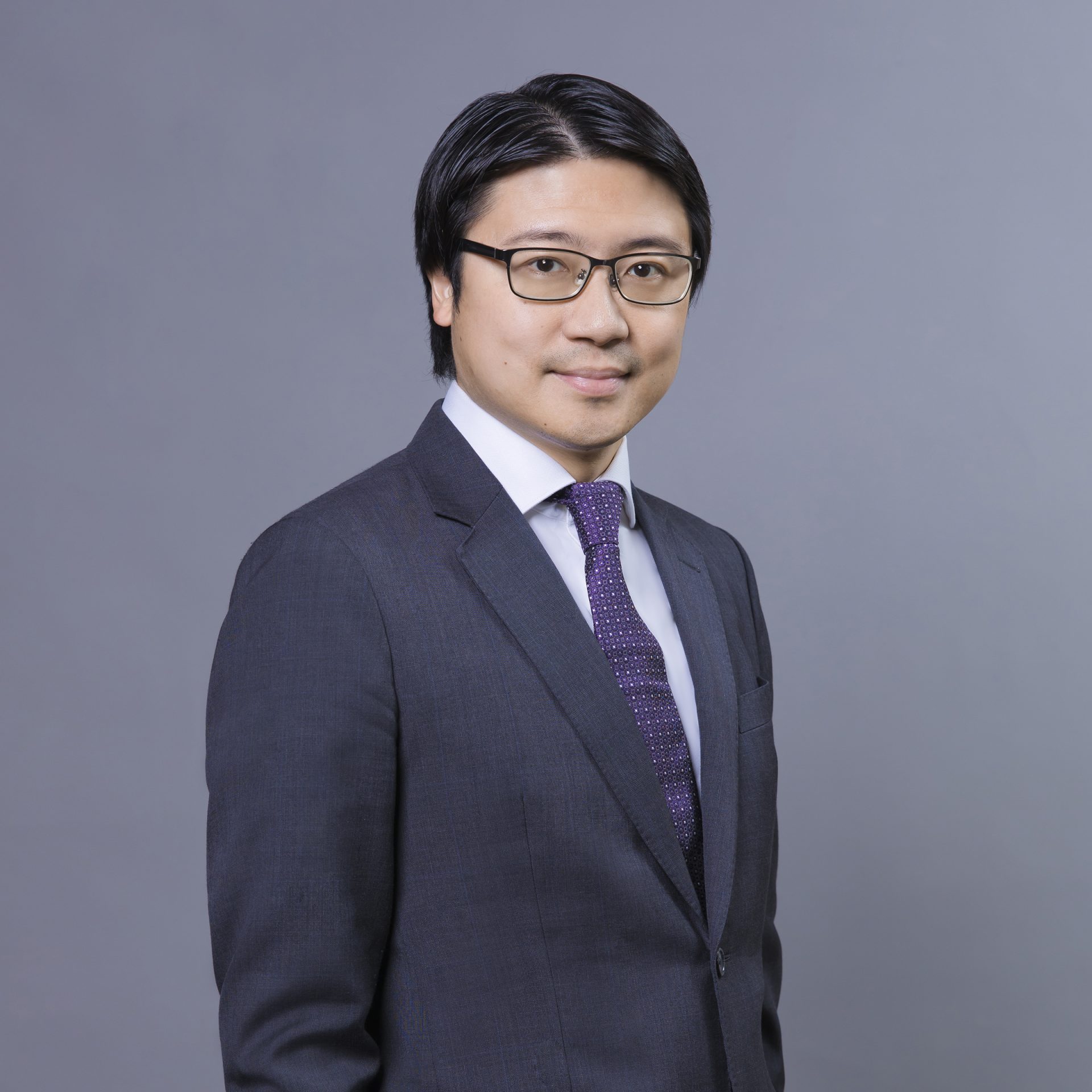Professional headshot of a man wearing glasses, a dark suit, and a patterned purple tie.