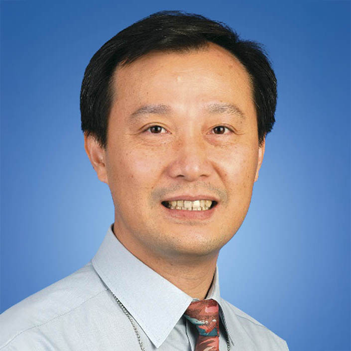 Portrait of Dr. Stephen Lam Wah Kwai, smiling, wearing light shirt and patterned tie against blue background.