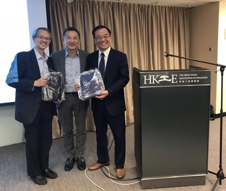 Three men in suits holding packaged smart devices at HKIE event