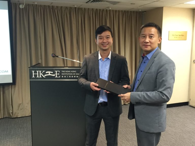 Two men in suits exchanging a black box at a podium for The Hong Kong Institution of Engineers.