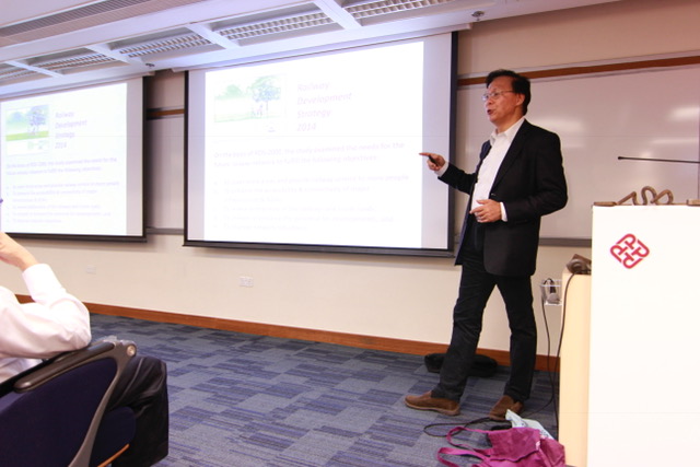 Man presenting slides on railway development strategy in a conference room.