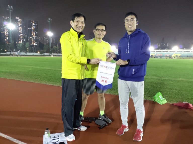 Three men on a running track at night holding a thank you banner.